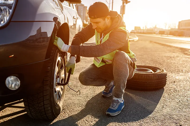 man changing tire on side of road